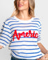 A woman wearing a white knit sweater with blue horizontal stripes and a large red 'America' script across the chest, shown against a light gray studio background.