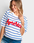A woman wearing a white short-sleeve knit sweater with blue horizontal stripes and a large red 'America' text graphic across the chest, paired with blue jeans against a light gray background.