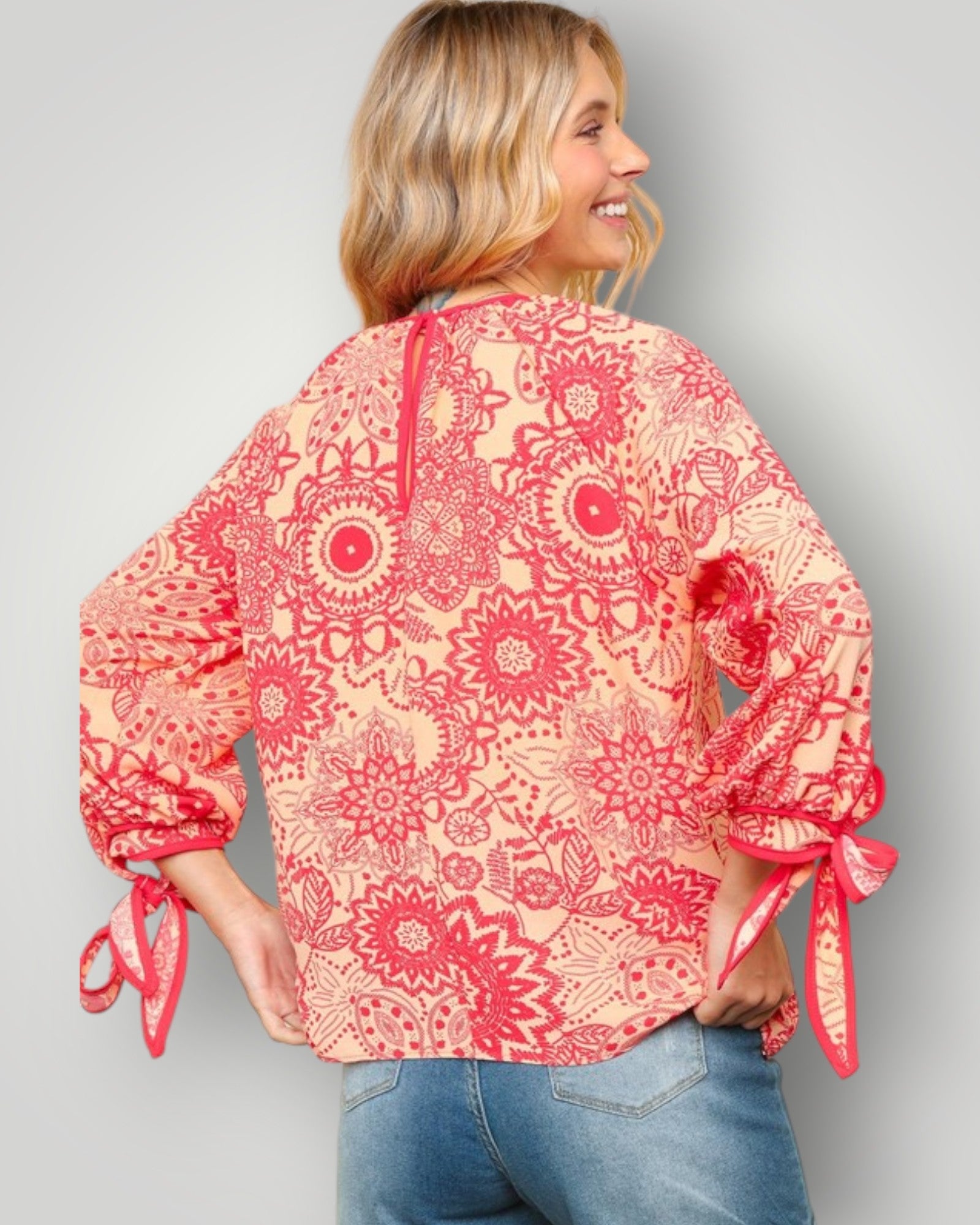 Woman wearing a red floral blouse with tied sleeves on a gray background