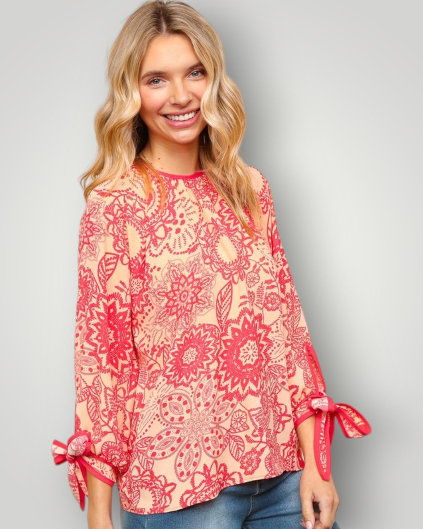 Woman wearing a red floral blouse with tied sleeves on a gray background