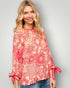 Woman wearing a red floral blouse with tied sleeves on a gray background