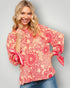 Woman wearing a red and pink floral blouse with tied sleeves on a gray background
