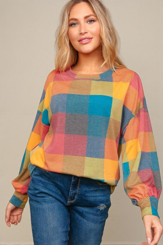 Woman wearing a colorful checkered sweater and blue jeans against a neutral background