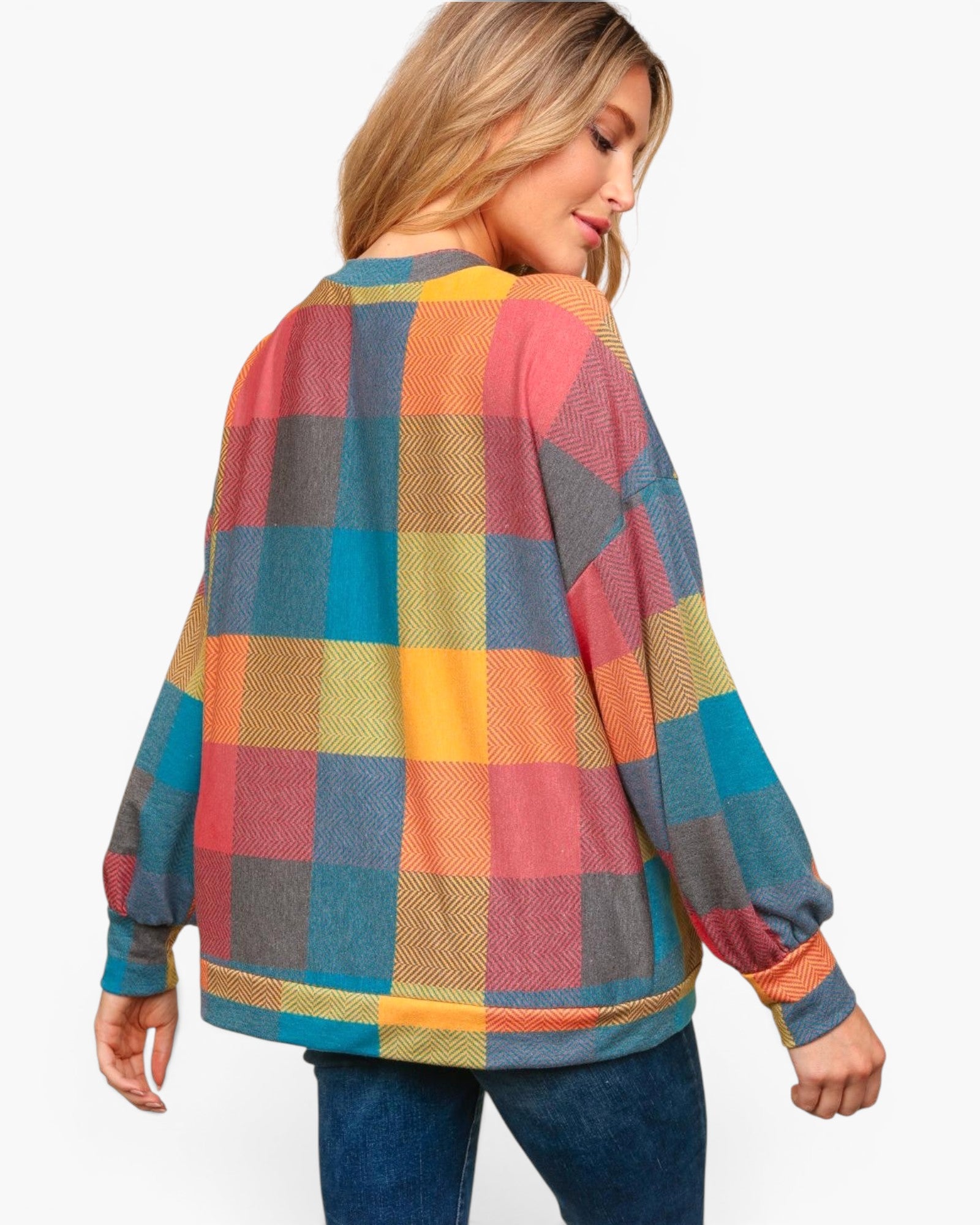 A woman shown from the back wearing a loose long-sleeve plaid sweater with a multicolor check pattern in blue, red, yellow, and gray, paired with blue jeans against a light gray studio background.