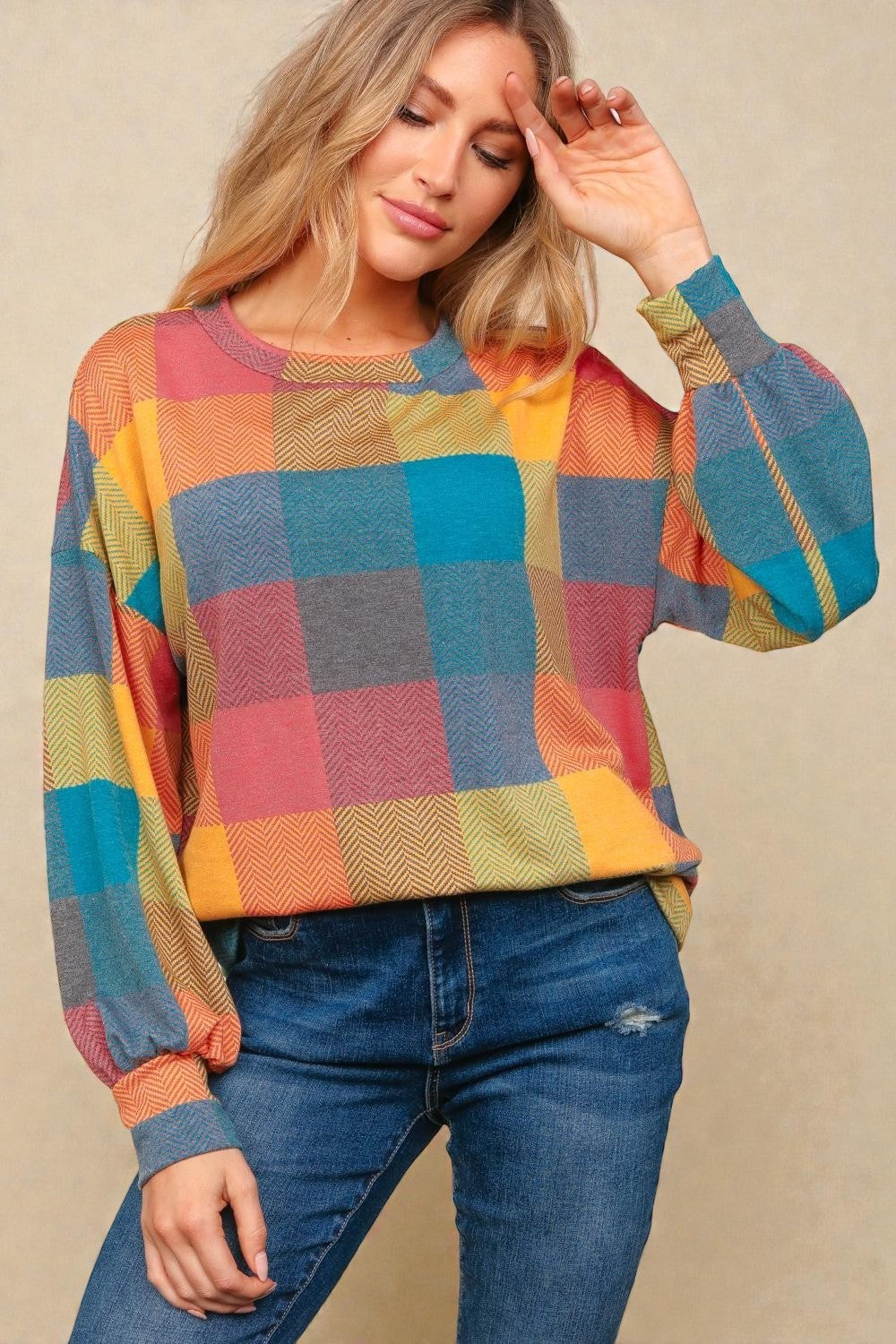 Woman wearing a colorful checkered sweater and blue jeans against a beige background