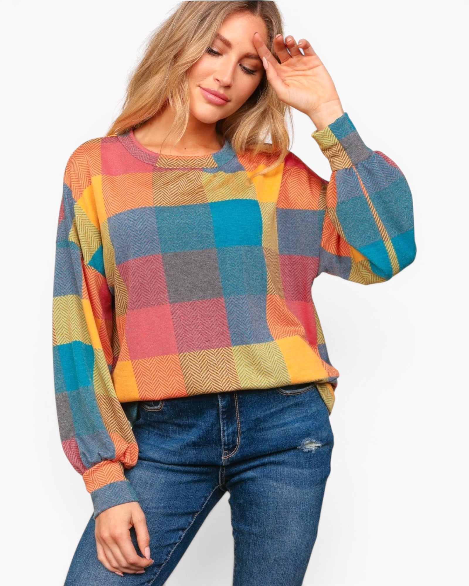 A woman wearing a colorful plaid long-sleeve knit top with blue jeans, posing against a light gray studio background.