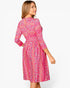 A woman wearing a pink floral long-sleeve dress, shown from the back and side against a plain white studio background.