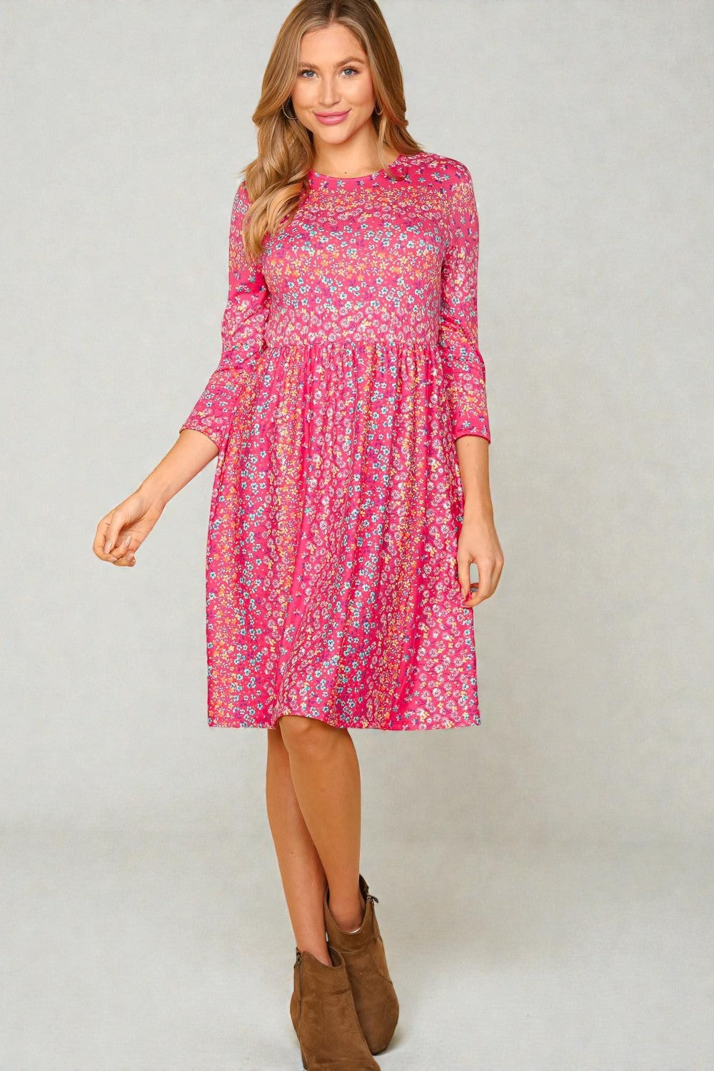 Woman wearing a pink floral dress with long sleeves on a plain background