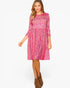 A woman modeling a pink and red floral print three-quarter sleeve dress with a gathered waist, paired with brown ankle boots, against a plain white background.