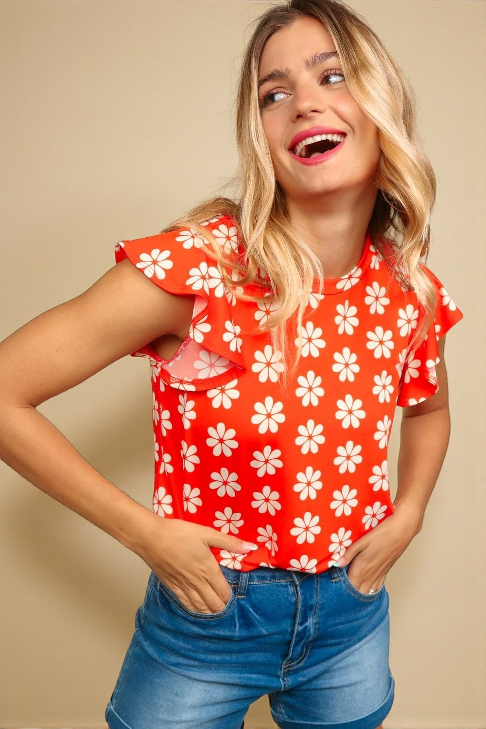 Woman wearing a red floral top and blue jeans against a beige background