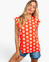 A woman modeling a bright red short-sleeve top with a white daisy floral pattern, paired with denim shorts, against a plain white studio background.