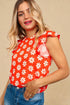Woman wearing a red top with white floral pattern against a beige background
