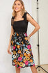 Woman wearing a black top with colorful floral skirt against a white background