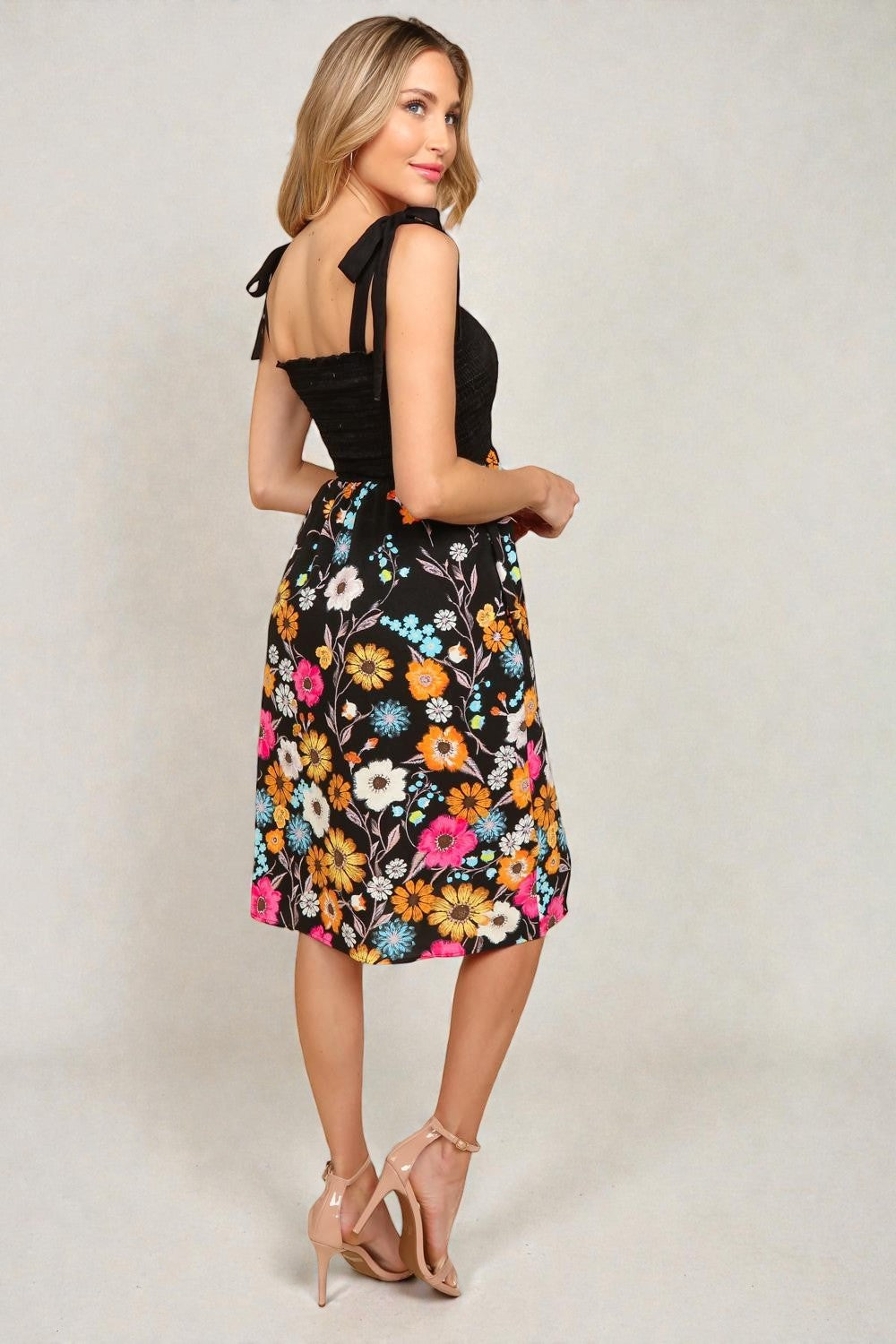 Woman wearing a black top and colorful floral skirt on a plain background