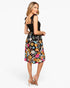 A woman modeling a black midi dress with a colorful floral print skirt and a black halter-style top, shown from a three-quarter back angle against a light gray studio background.