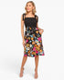 A woman modeling a sleeveless midi dress with a black smocked bodice and a vibrant multicolor floral print skirt, set against a plain light gray studio background.