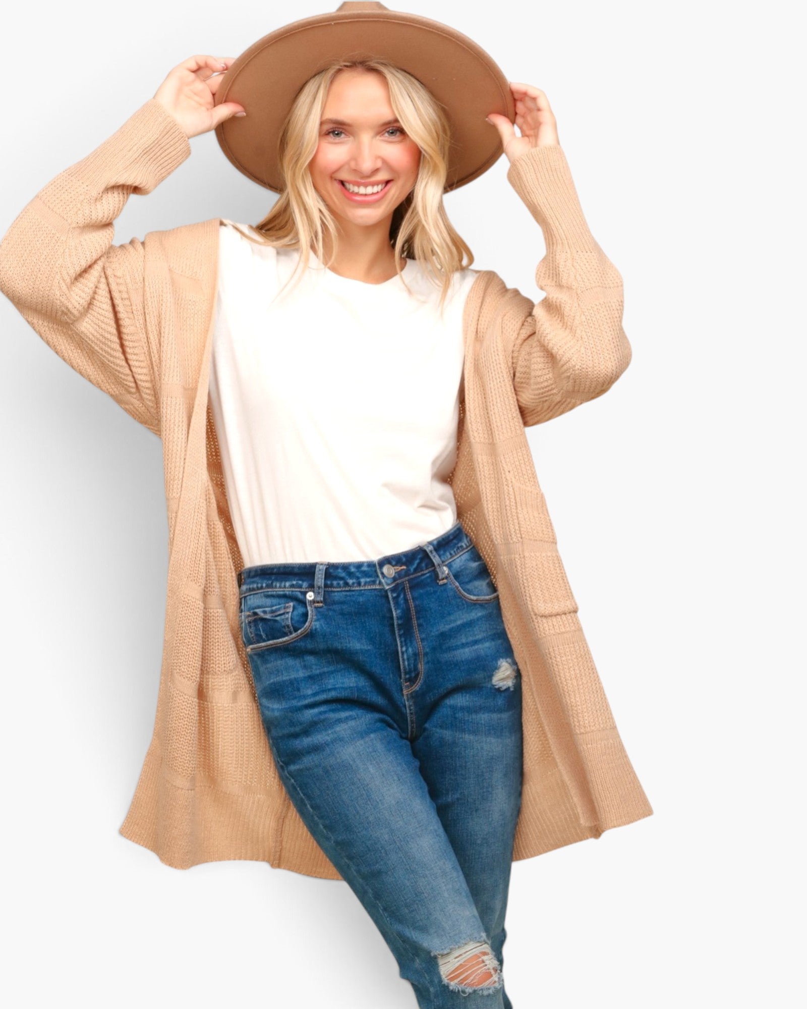 A woman modeling a beige open-front knit cardigan over a white t-shirt and blue jeans, wearing a wide-brim tan hat against a light gray background.