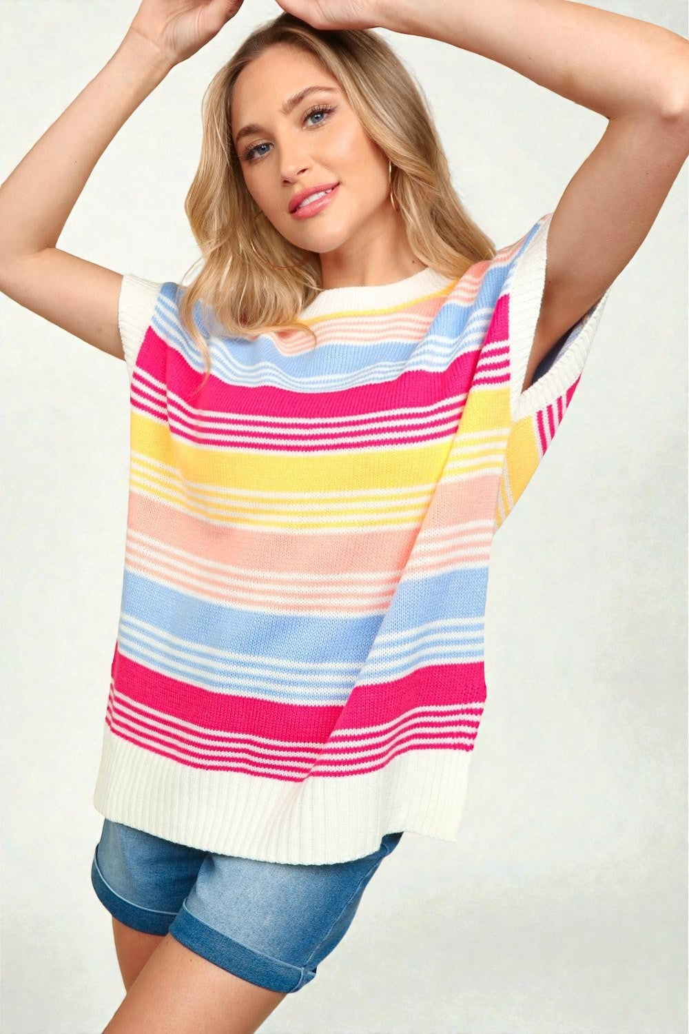 Woman wearing a colorful striped sweater and denim shorts on a plain background