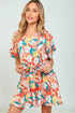 Woman wearing a colorful floral romper against a plain background