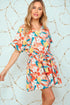 Woman wearing a colorful floral romper against a light blue background with gold circular patterns.