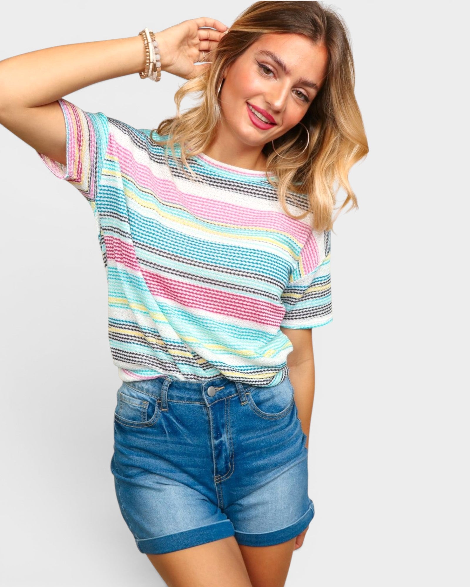 Woman wearing a colorful striped shirt and blue shorts on a plain background
