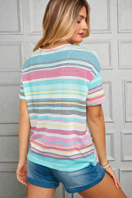 Woman wearing a colorful striped shirt and denim shorts against a gray wall.