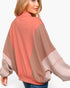A woman wearing a color-blocked sweatshirt with a coral pink upper section, taupe-brown middle panels, and light pink lower sleeves and hem, shown from a three-quarters back view against a light gray studio background.