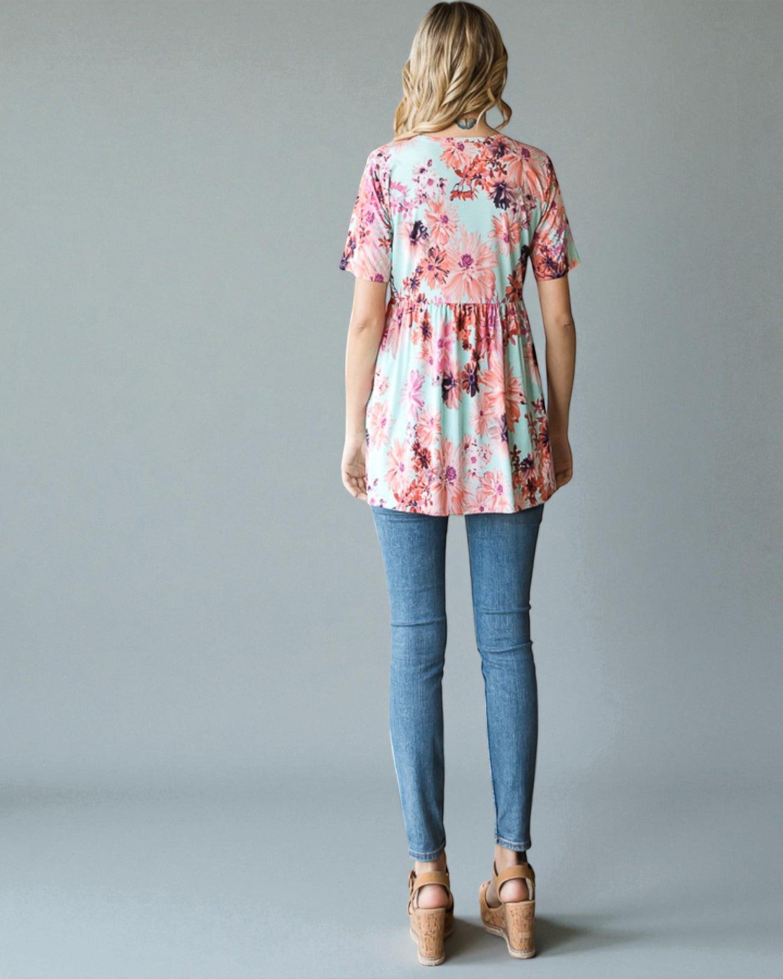 Woman wearing a floral blouse and blue jeans on a gray background