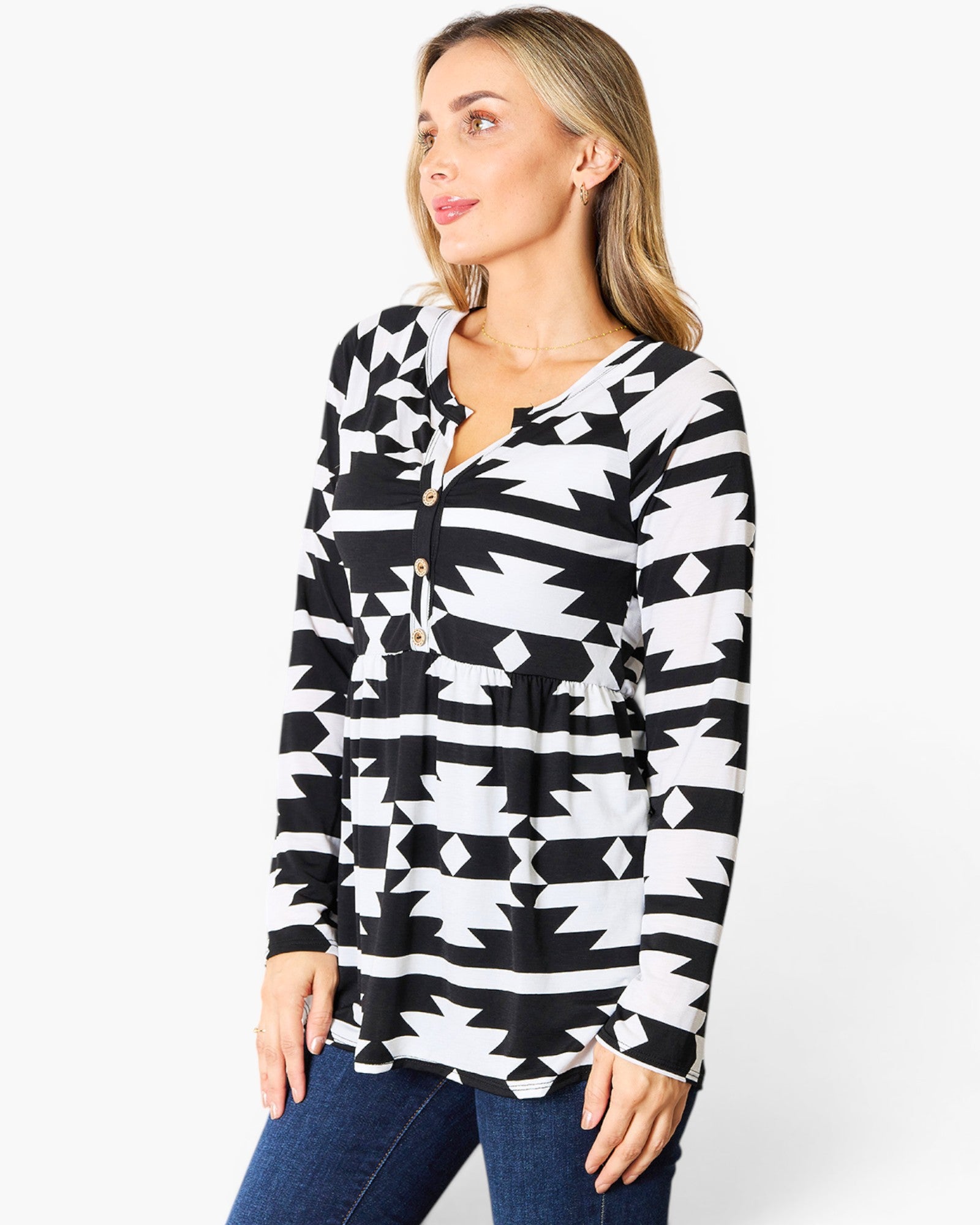A woman wearing a black and white geometric patterned long-sleeve top with a split neckline and drawstring, paired with blue jeans, against a plain white studio background.