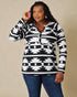 Woman wearing a black and white patterned top with blue jeans against a beige background