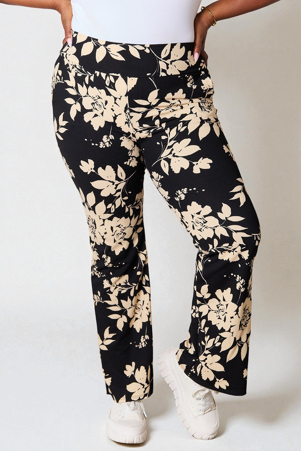 Person wearing black pants with beige floral pattern on a white background