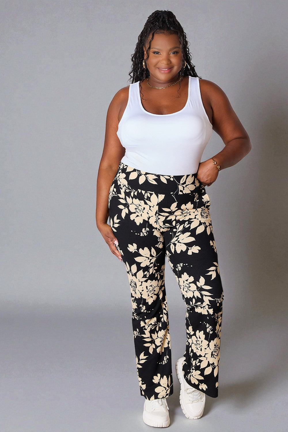 Woman wearing a white tank top and black floral pants on a gray background