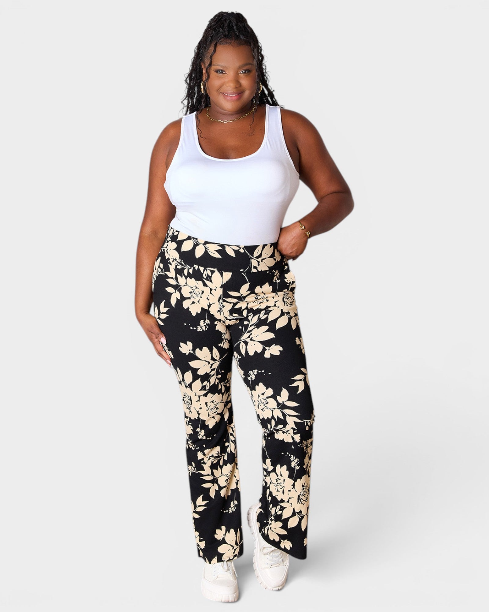 Woman wearing a white tank top and black floral pants on a white background
