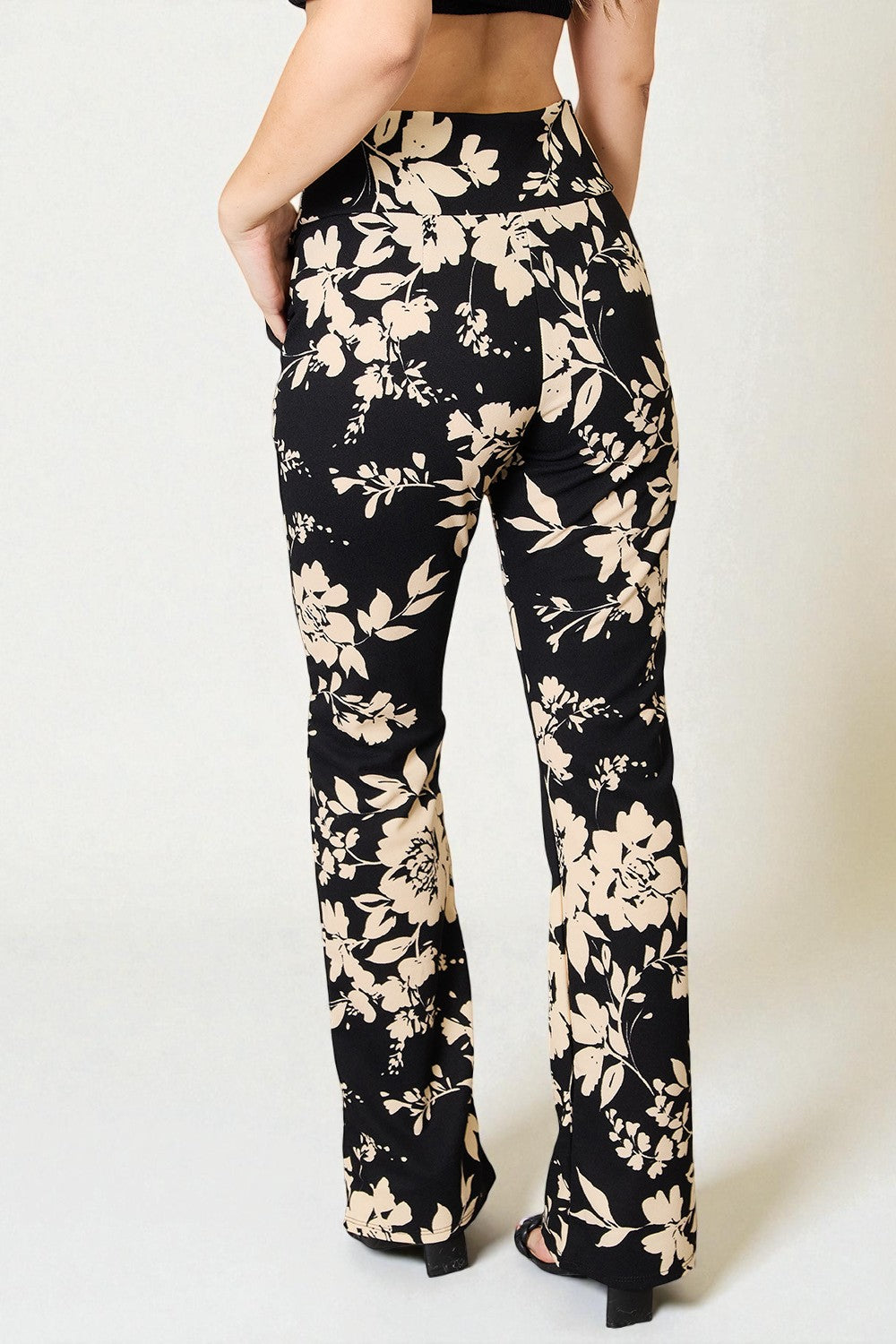 Black pants with beige floral pattern worn by a person on a white background