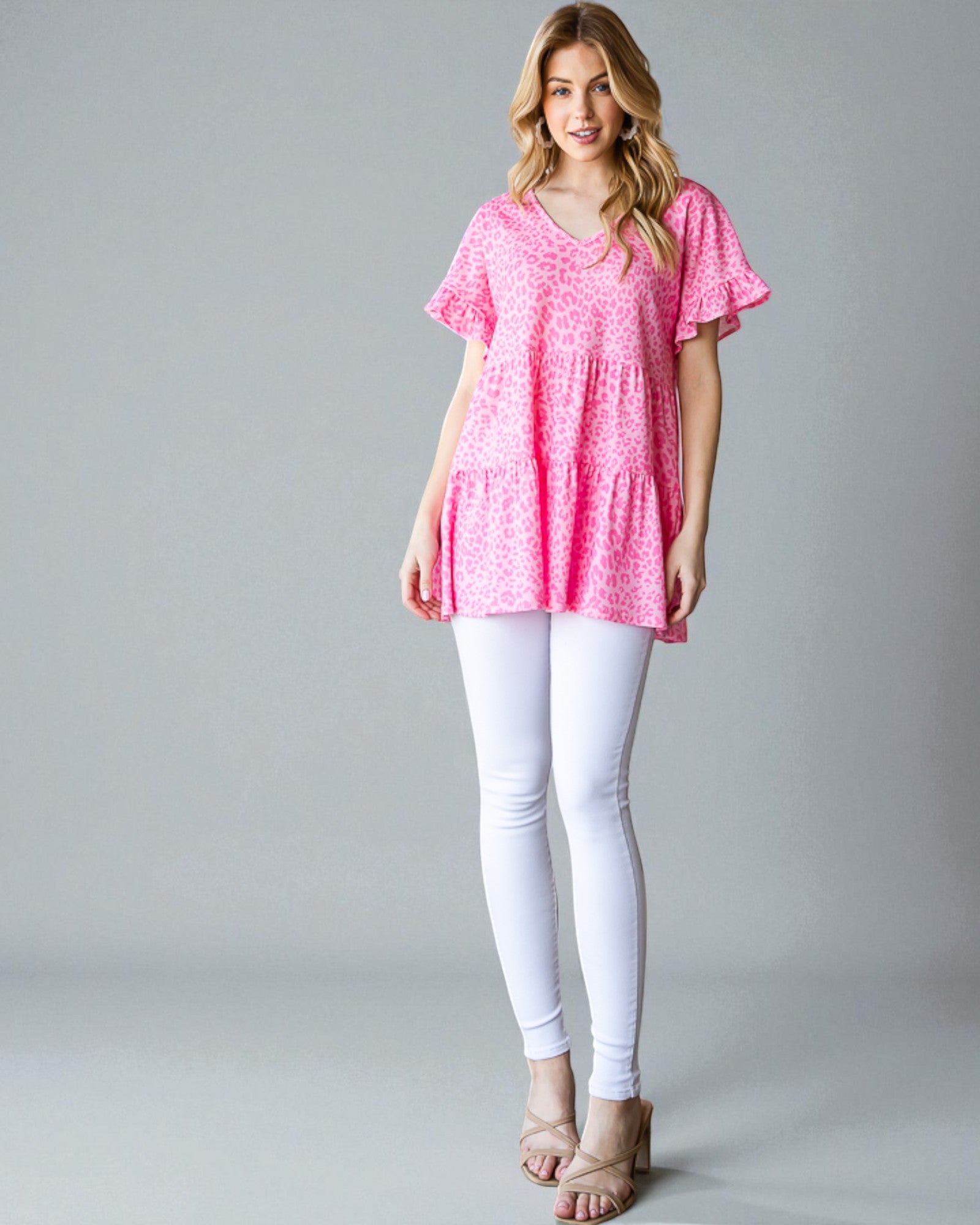 Woman wearing a pink floral top and white pants on a gray background