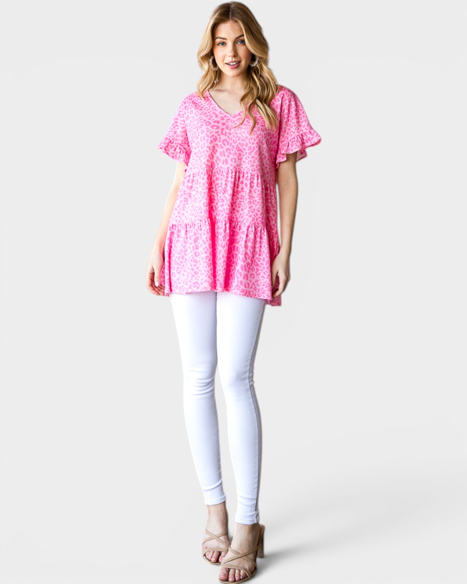 Woman wearing a pink patterned top and white pants on a light gray background