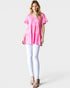 Woman wearing a pink patterned top and white pants on a light gray background
