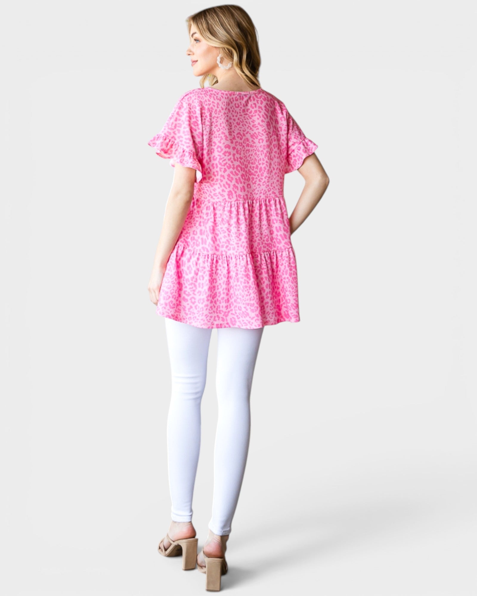 Woman wearing a pink floral dress with white pants on a light gray background