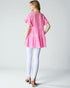 Woman wearing a pink floral dress and white leggings on a plain background