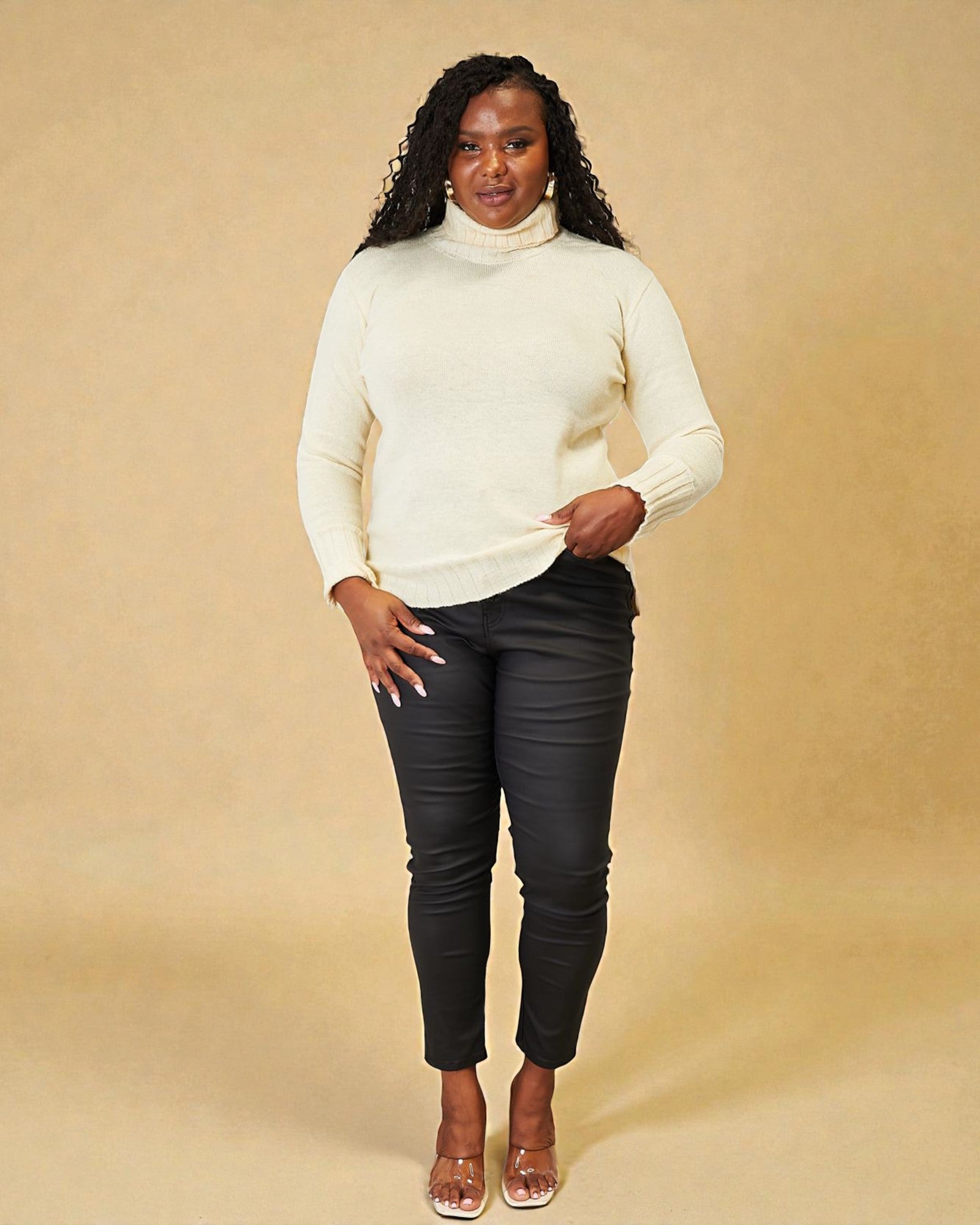 Woman wearing a white sweater and black pants against a beige background