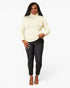 A woman modeling a cream turtleneck sweater and black skinny jeans against a plain white studio background.