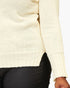 Close-up of a cream-colored knit sweater worn by a model, paired with black pants, against a plain white background.