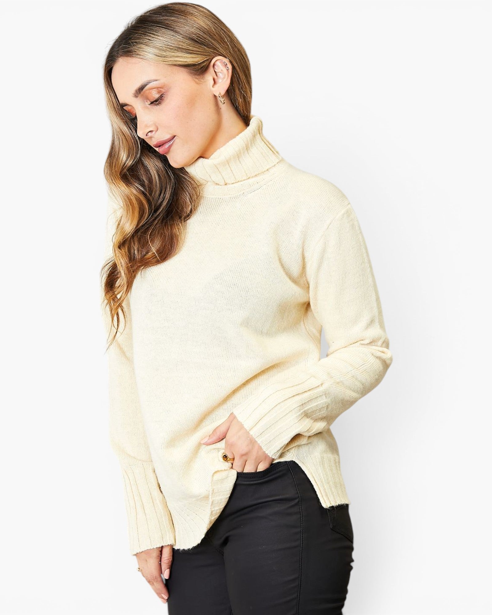 A woman wearing a cream-colored ribbed mock neck sweater and black pants, photographed against a plain white studio background.
