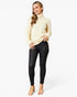 A woman modeling a cream-colored mock neck knit sweater and black skinny jeans against a plain white studio background.