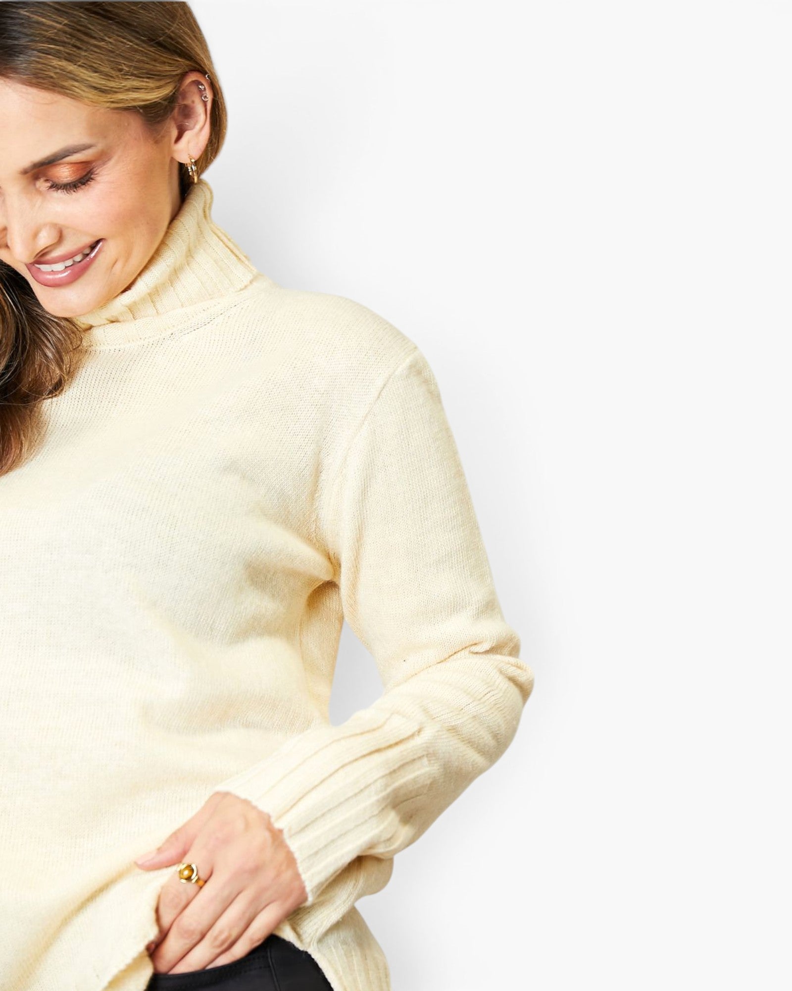 A woman wearing a cream-colored ribbed turtleneck sweater, shown from the side against a plain white background.