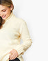 A woman wearing a cream-colored ribbed turtleneck sweater, shown from the side against a plain white background.