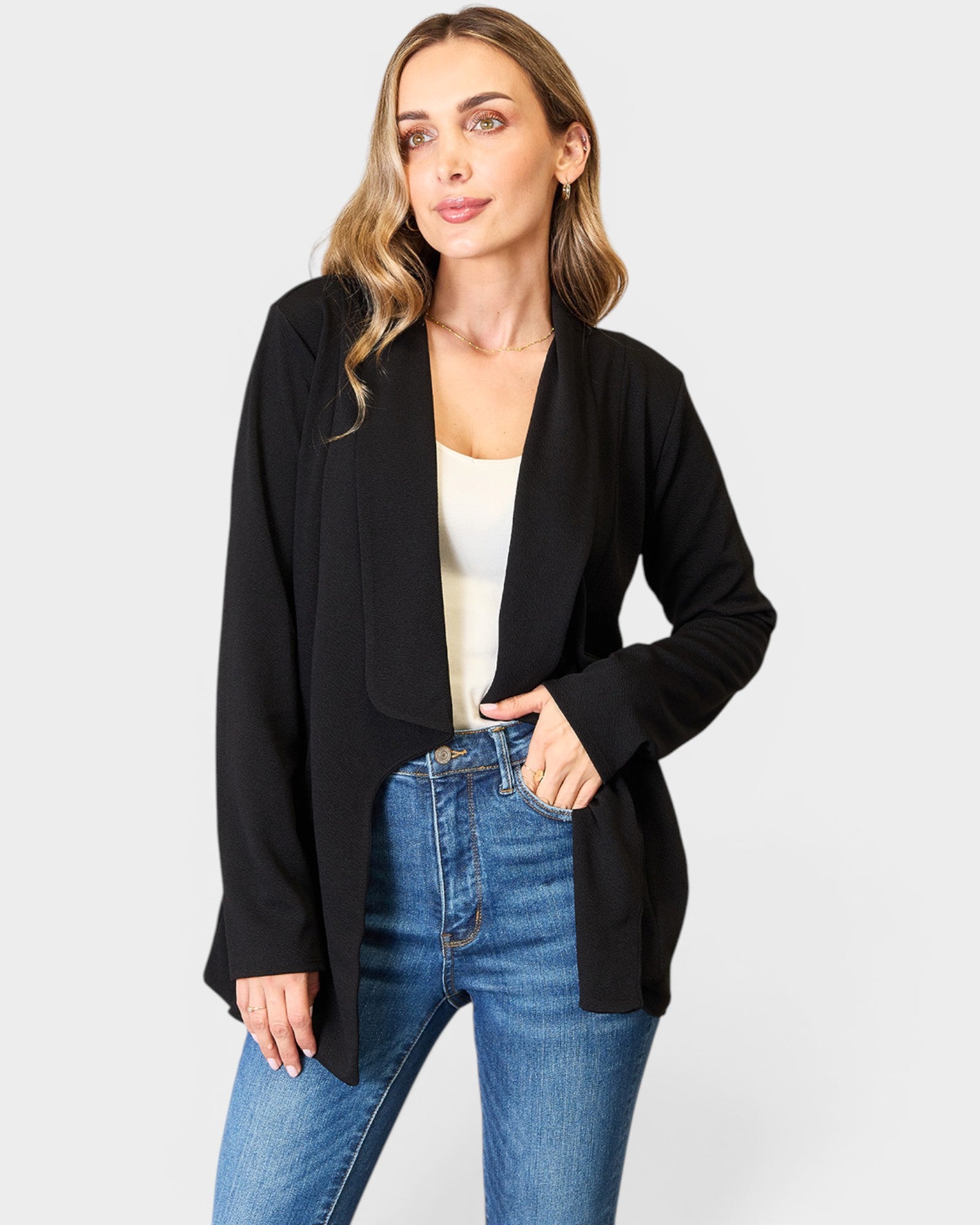 Woman wearing a black blazer and blue jeans on a white background