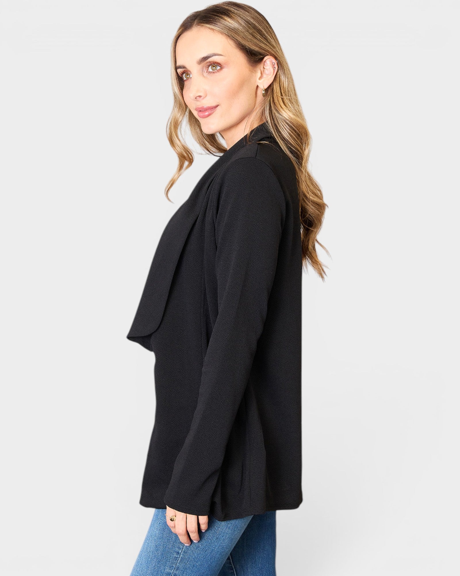Woman wearing a black blazer and blue jeans on a white background