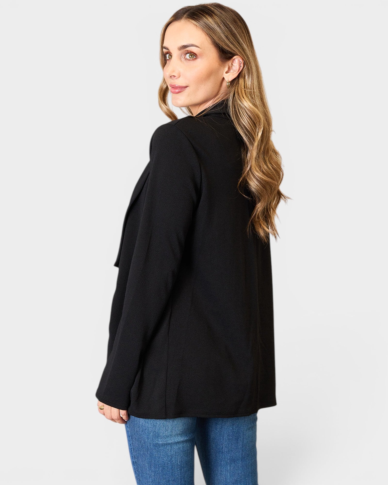 Woman wearing a black blazer and blue jeans on a white background