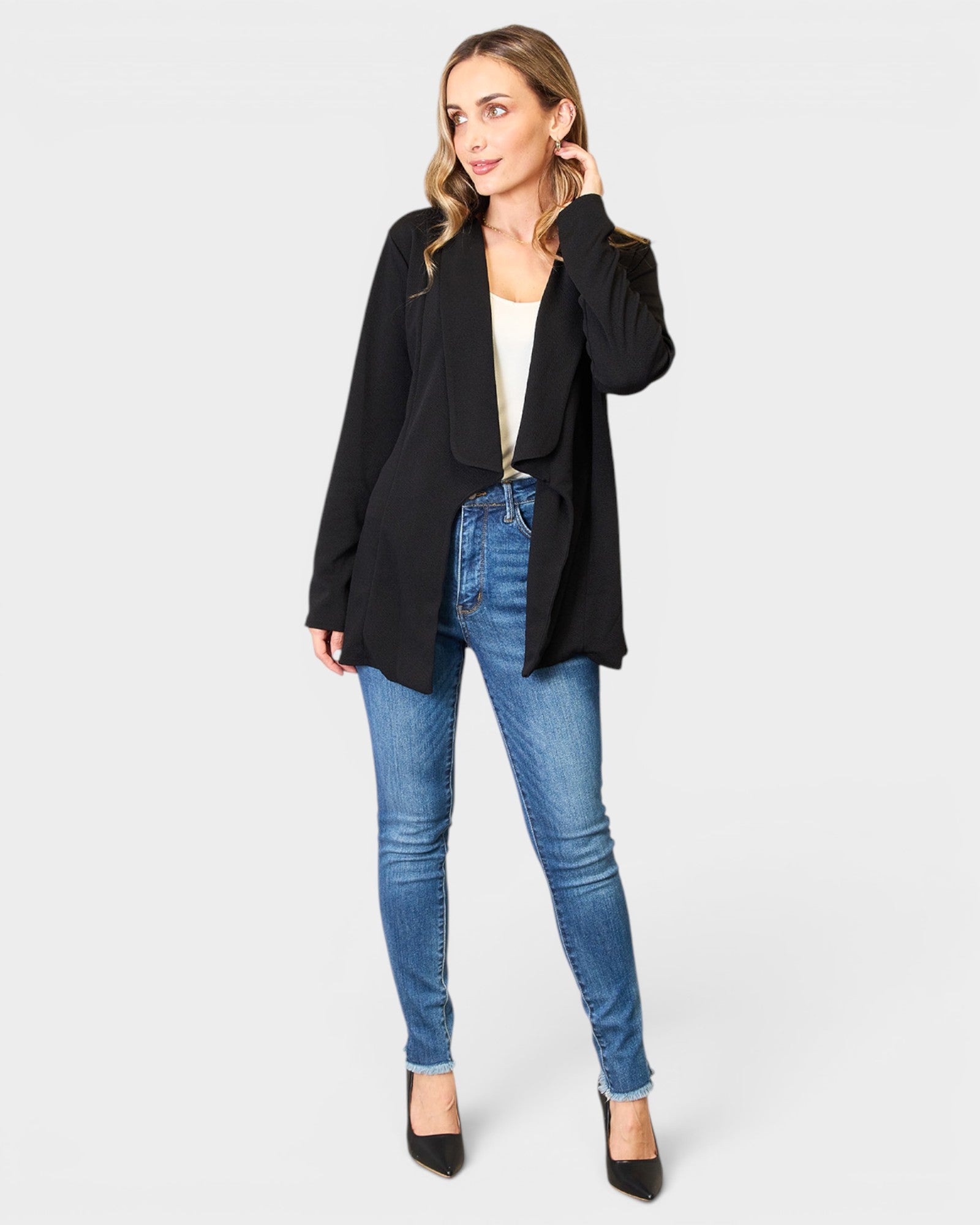 Woman wearing a black blazer and blue jeans on a white background